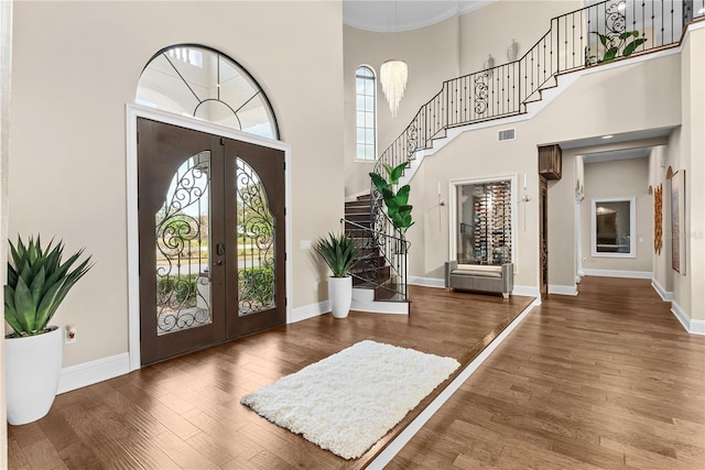 entrance foyer with french doors, hardwood / wood-style floors, ornamental molding, and a high ceiling