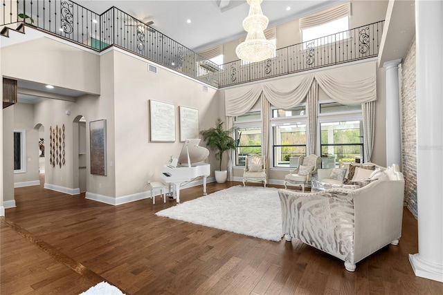 living room with dark wood-type flooring, ornate columns, a chandelier, and a high ceiling