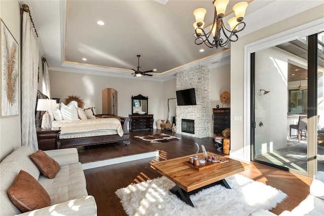 bedroom featuring a fireplace, a raised ceiling, ornamental molding, dark hardwood / wood-style flooring, and a chandelier