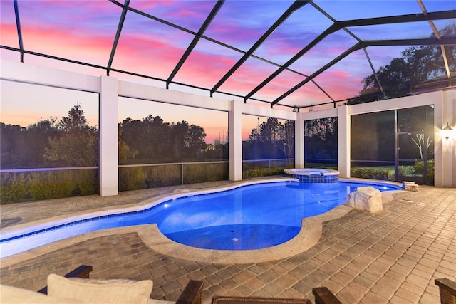 pool at dusk featuring a patio, glass enclosure, and an in ground hot tub