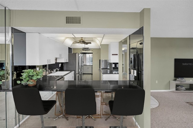 kitchen with white cabinets, kitchen peninsula, stainless steel fridge, and light colored carpet