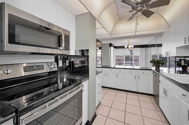 kitchen featuring sink, light tile patterned floors, stainless steel appliances, white cabinets, and ceiling fan with notable chandelier