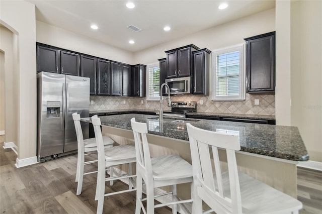 kitchen featuring stainless steel appliances, a kitchen breakfast bar, dark stone counters, and an island with sink