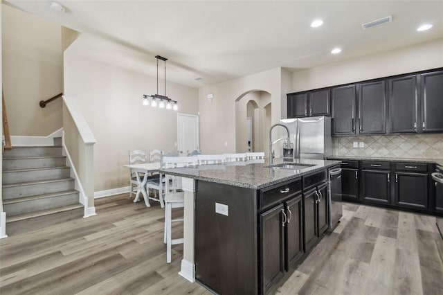 kitchen with appliances with stainless steel finishes, an island with sink, sink, decorative light fixtures, and tasteful backsplash