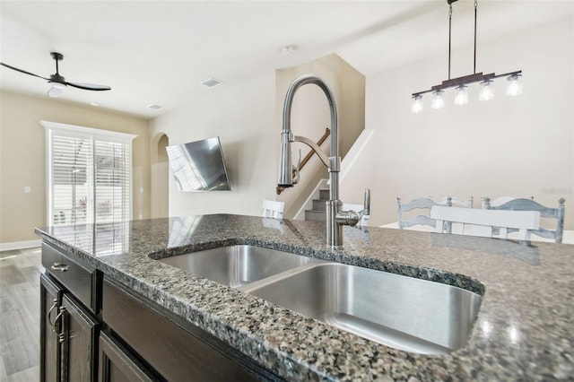 kitchen with hardwood / wood-style floors, dark stone counters, pendant lighting, ceiling fan, and sink