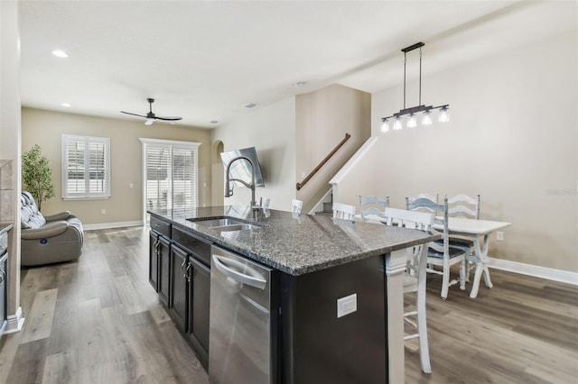 kitchen featuring stainless steel dishwasher, decorative light fixtures, a kitchen island with sink, dark stone counters, and sink