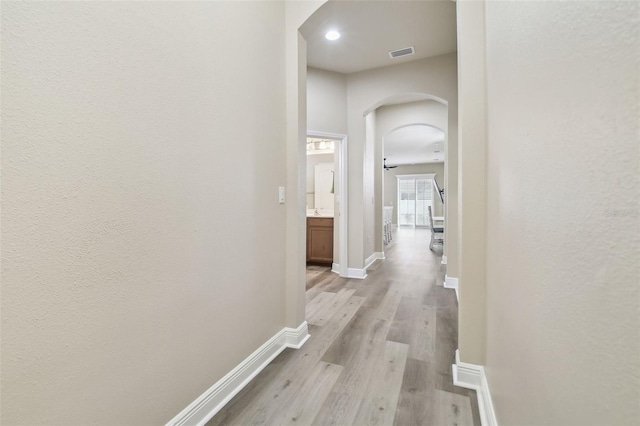 hall with light wood-type flooring, visible vents, arched walkways, and baseboards