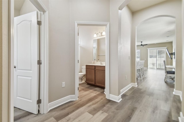 hall featuring light wood-style flooring, baseboards, and arched walkways