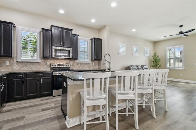 kitchen with light wood finished floors, a center island with sink, appliances with stainless steel finishes, and a kitchen bar