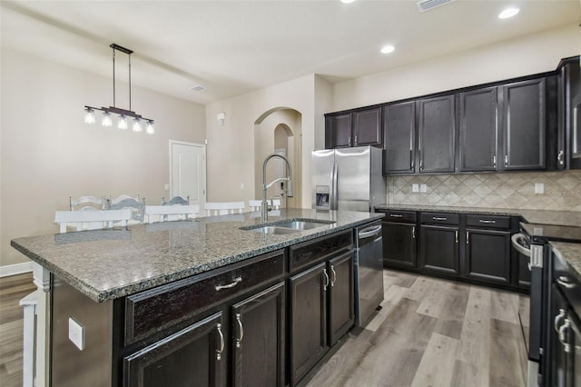 kitchen featuring a center island with sink, a sink, stainless steel appliances, light wood-style floors, and decorative backsplash