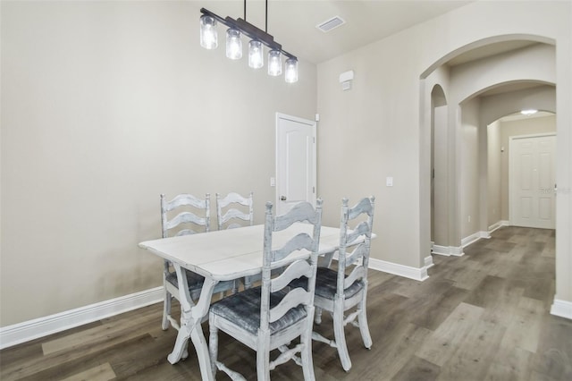 dining area featuring baseboards, arched walkways, visible vents, and wood finished floors