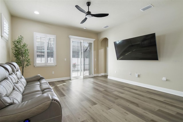 unfurnished living room featuring arched walkways, visible vents, a healthy amount of sunlight, and wood finished floors