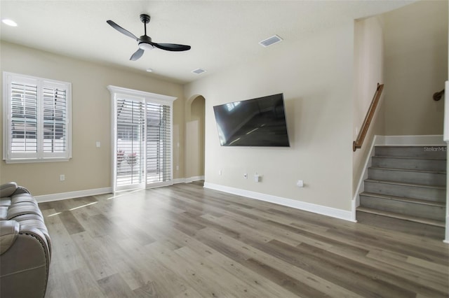 unfurnished living room featuring visible vents, a ceiling fan, wood finished floors, stairway, and baseboards