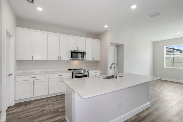 kitchen with an island with sink, appliances with stainless steel finishes, wood finished floors, white cabinetry, and a sink