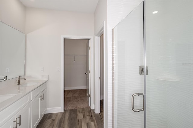 full bath featuring a spacious closet, a stall shower, a sink, wood finished floors, and baseboards