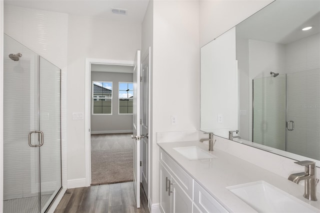 bathroom featuring double vanity, wood finished floors, a sink, and a shower stall