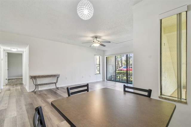 unfurnished dining area with ceiling fan with notable chandelier, a textured ceiling, and light hardwood / wood-style floors