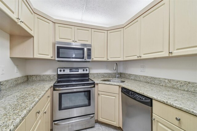 kitchen with sink, stainless steel appliances, light tile patterned flooring, and light stone countertops