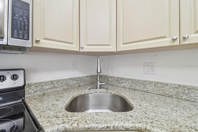 room details featuring light stone counters, stainless steel appliances, cream cabinets, and sink