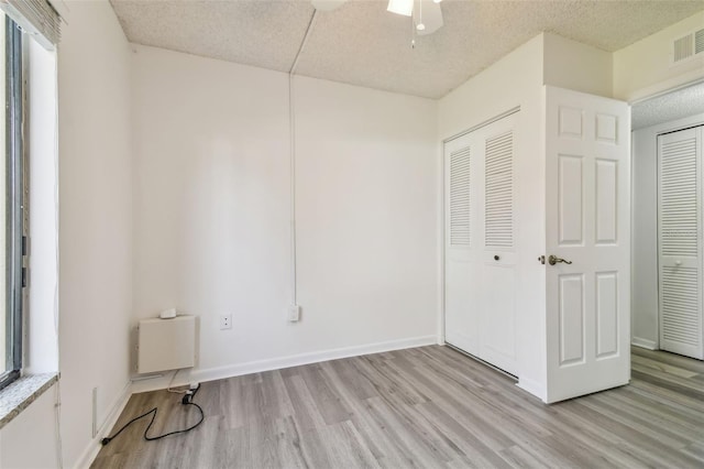 unfurnished bedroom with a textured ceiling, ceiling fan, light wood-type flooring, a closet, and multiple windows