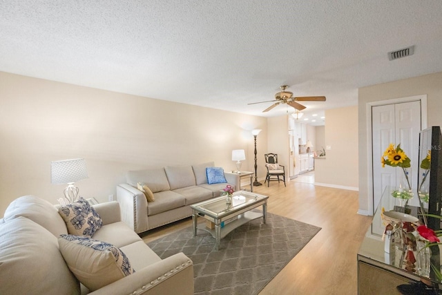 living room featuring hardwood / wood-style flooring, ceiling fan, and a textured ceiling