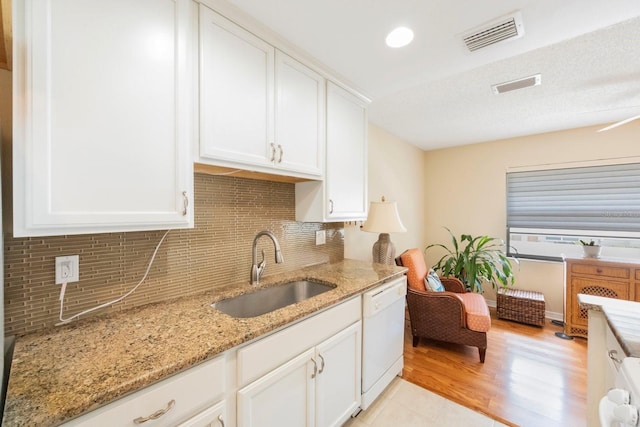 kitchen with white cabinetry, sink, light stone countertops, backsplash, and white dishwasher