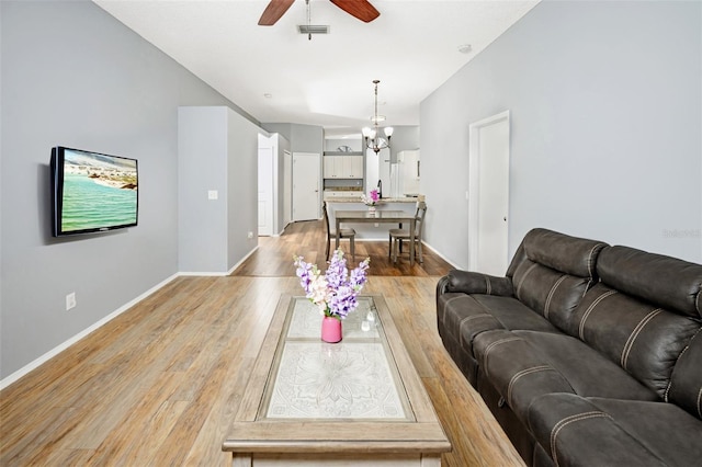 living room with light wood-type flooring and ceiling fan with notable chandelier