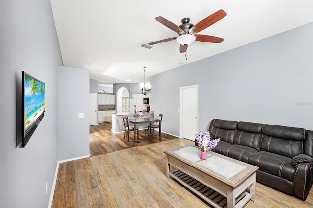 living room with ceiling fan with notable chandelier, light hardwood / wood-style floors, and sink