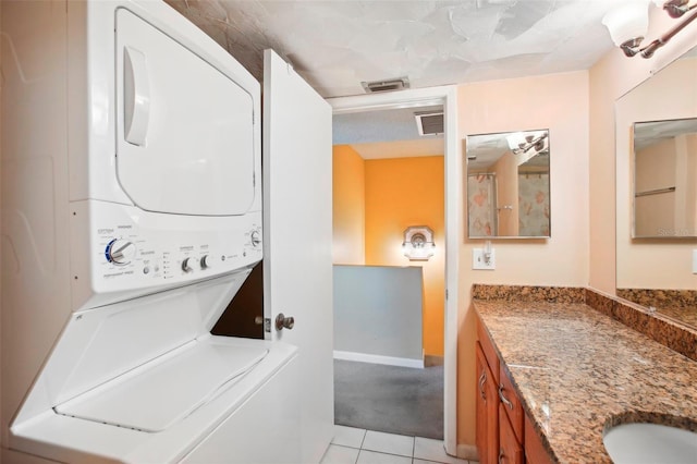 laundry room featuring stacked washer / drying machine, light tile patterned floors, and sink