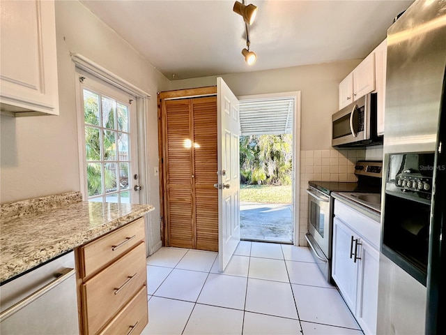 kitchen with white cabinetry, appliances with stainless steel finishes, light tile patterned flooring, track lighting, and light stone counters