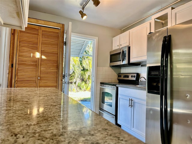 kitchen with decorative backsplash, white cabinetry, light stone countertops, stainless steel appliances, and rail lighting