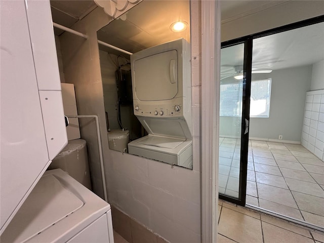 laundry area with ceiling fan, stacked washer / dryer, and light tile patterned floors