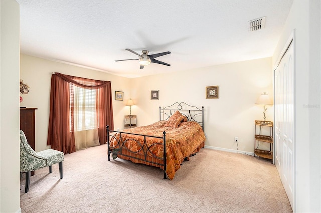 bedroom with a textured ceiling, ceiling fan, a closet, and light carpet