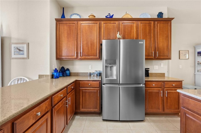 kitchen with light tile patterned flooring, light stone countertops, and stainless steel refrigerator with ice dispenser