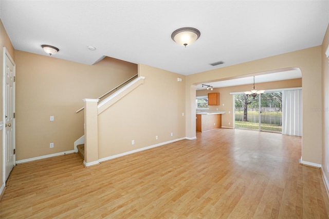 unfurnished living room with plenty of natural light, light hardwood / wood-style flooring, and an inviting chandelier