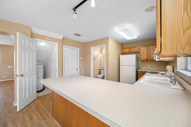 kitchen with white fridge, kitchen peninsula, stove, light hardwood / wood-style flooring, and sink