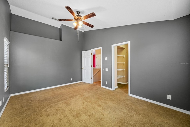 unfurnished bedroom featuring ceiling fan, light colored carpet, vaulted ceiling, a spacious closet, and a closet