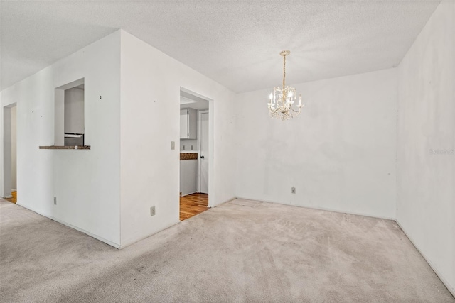 carpeted empty room with a textured ceiling and a notable chandelier