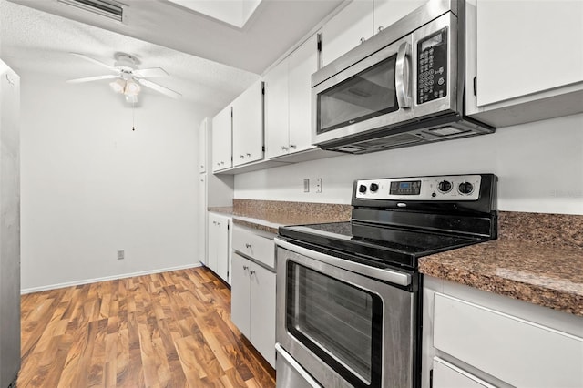 kitchen featuring light wood-type flooring, a textured ceiling, stainless steel appliances, and white cabinetry