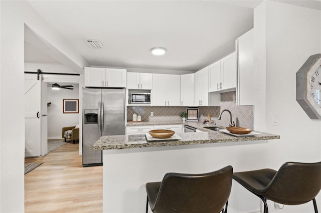 kitchen featuring a barn door, kitchen peninsula, appliances with stainless steel finishes, and light stone counters