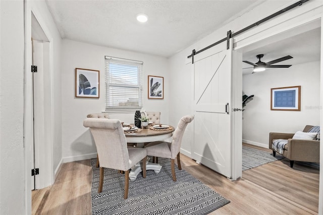 dining space with ceiling fan, a barn door, light wood-type flooring, and a textured ceiling