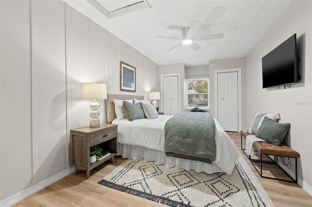 bedroom with ceiling fan, multiple closets, and light hardwood / wood-style flooring