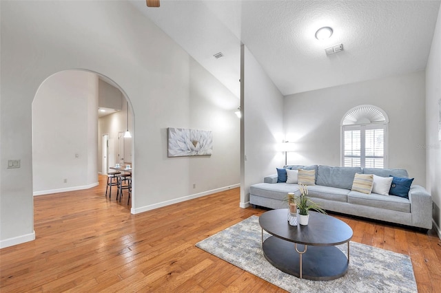 living room featuring a textured ceiling, light hardwood / wood-style flooring, and high vaulted ceiling