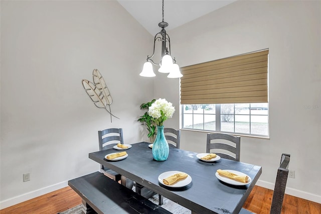 dining space with hardwood / wood-style floors, lofted ceiling, and a notable chandelier