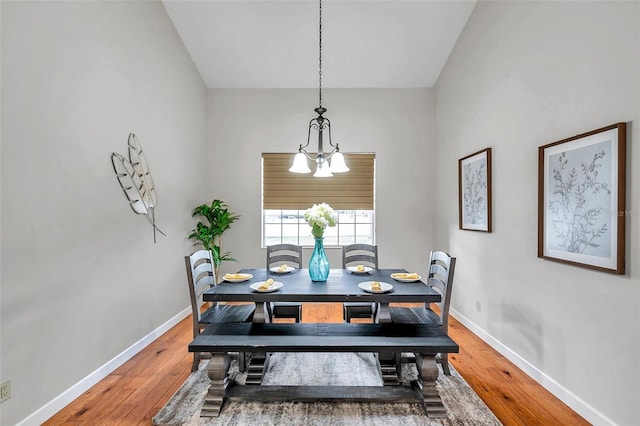 dining area with lofted ceiling, wood-type flooring, and a notable chandelier