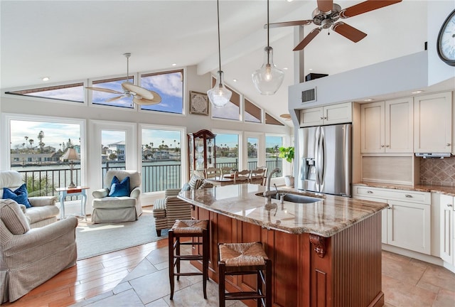 kitchen with stainless steel fridge, sink, light stone counters, and pendant lighting