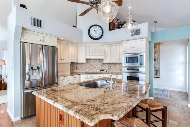 kitchen with appliances with stainless steel finishes, a center island with sink, light stone counters, and sink