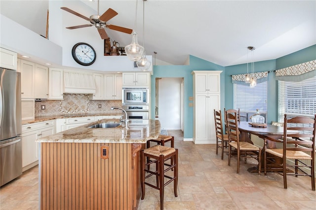 kitchen featuring an island with sink, stainless steel appliances, tasteful backsplash, light stone countertops, and sink