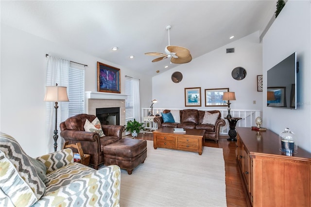 living room with light wood-type flooring, ceiling fan, a tiled fireplace, and high vaulted ceiling