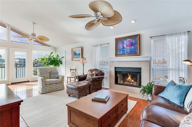 living room with ceiling fan, light hardwood / wood-style floors, lofted ceiling, and a tiled fireplace